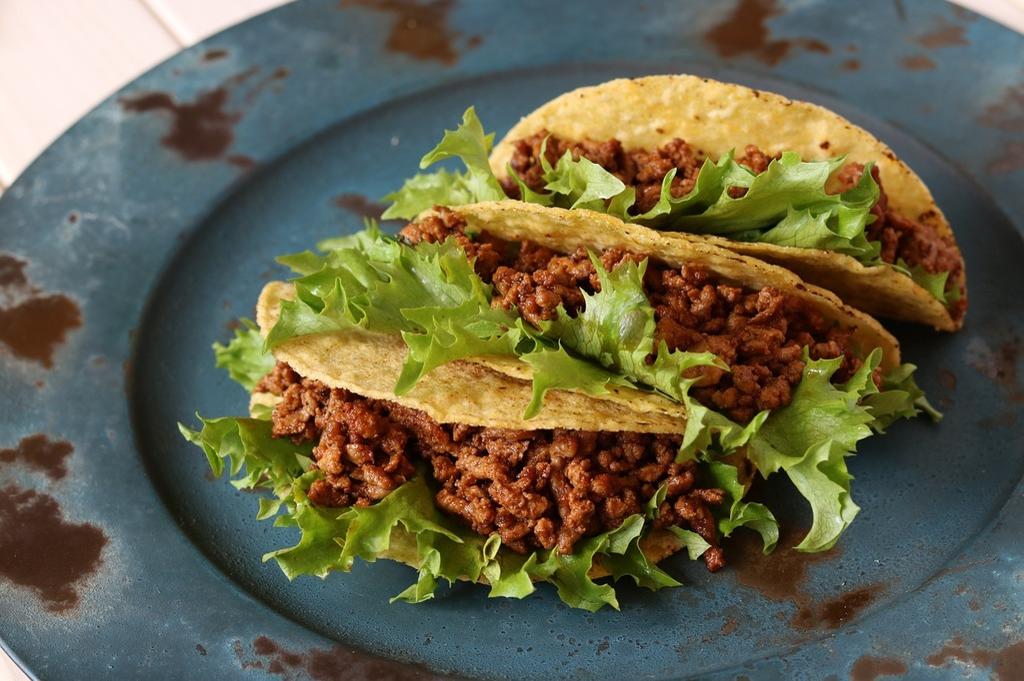 three homemade style hard shell tacos sit on a worn blue plate. Ample ground beef and whole leaf romaine lettuce make up the filling