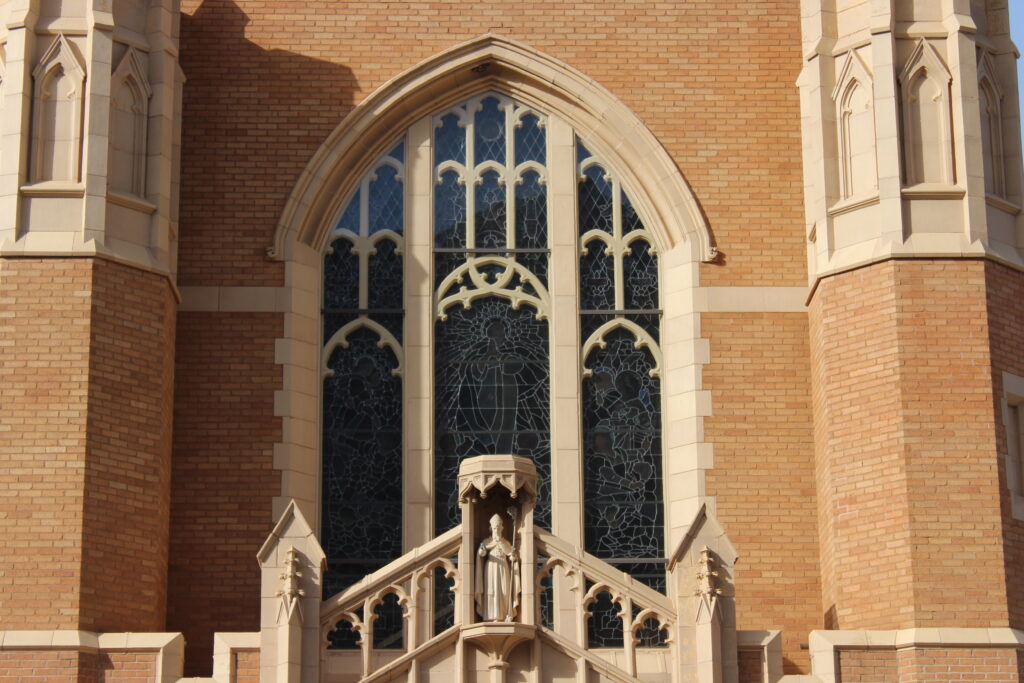 the front of st particks catholic curch in bisbee arizona. close up of the front window and its artwork, the main spires, and the image of St Patrick in a small tower