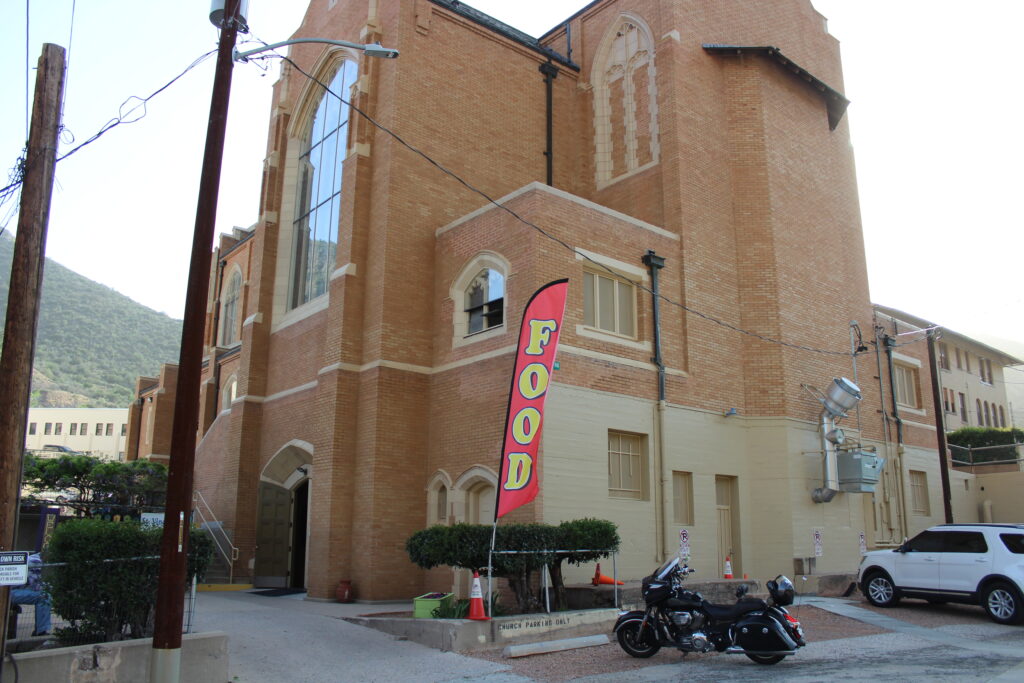backside of saint patricks church in bisbee. a feather flag says FOOD in red and yellow and a black motorcycle is parked adjacent